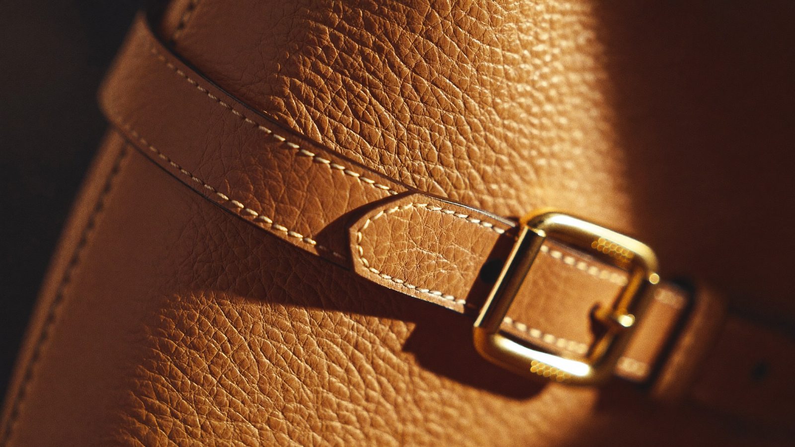 Close-up of pebbled leather texture with cream stitching and gold buckle